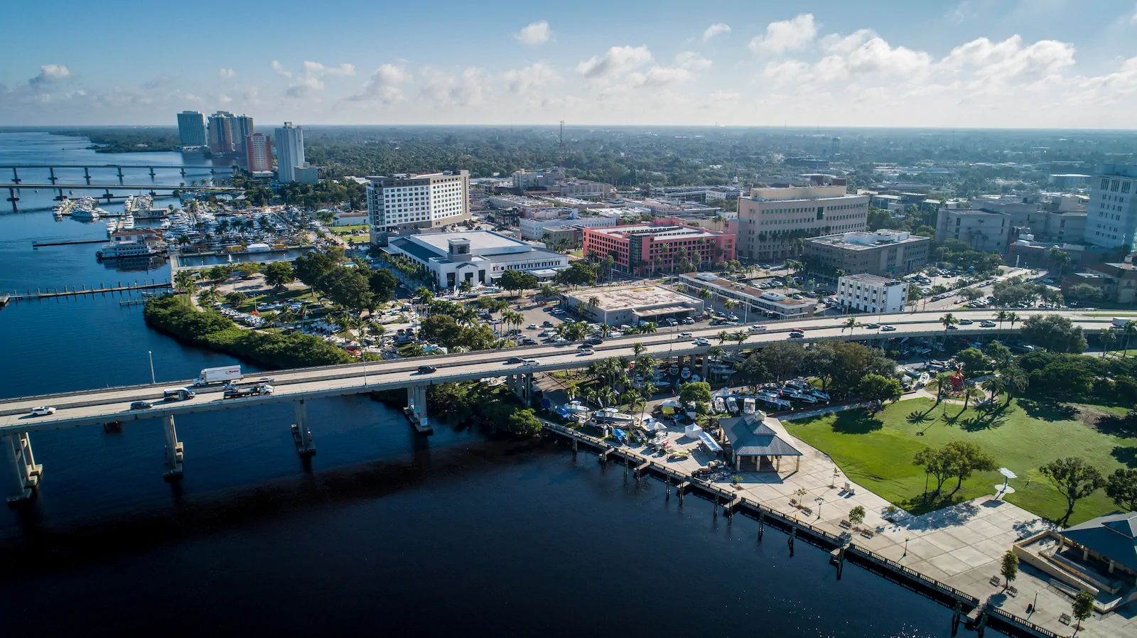 An aerial view of the Fort Myers riverfront: the downtown skyline, the marina, and the bridge carrying traffic across the Caloosahatchee.