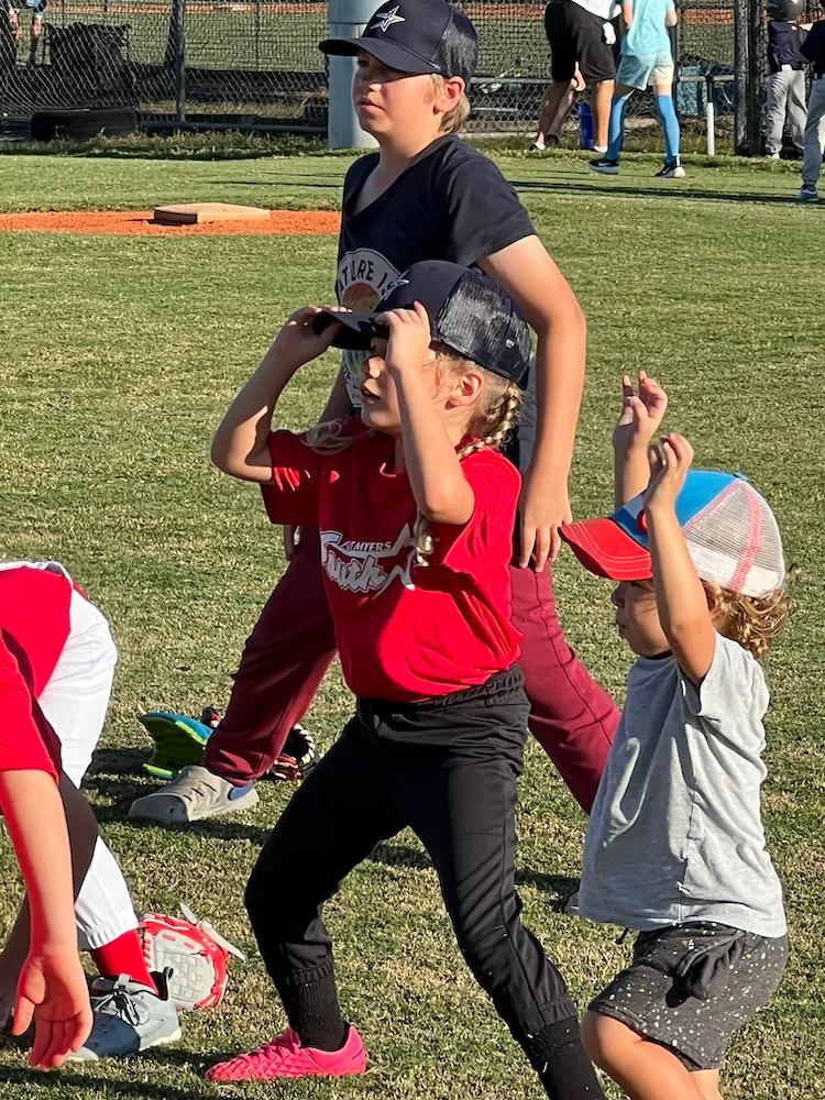 Kids on the outfield grass during a Lee County little-league game at golden hour.