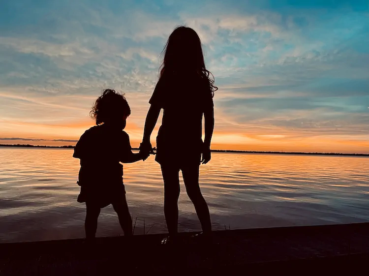 Two kids holding hands, silhouetted against a Caloosahatchee sunset over the water.