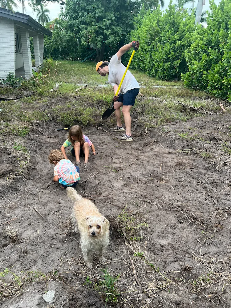 Elliot regrading the backyard with a shovel while his kids and the family dog pitch in.