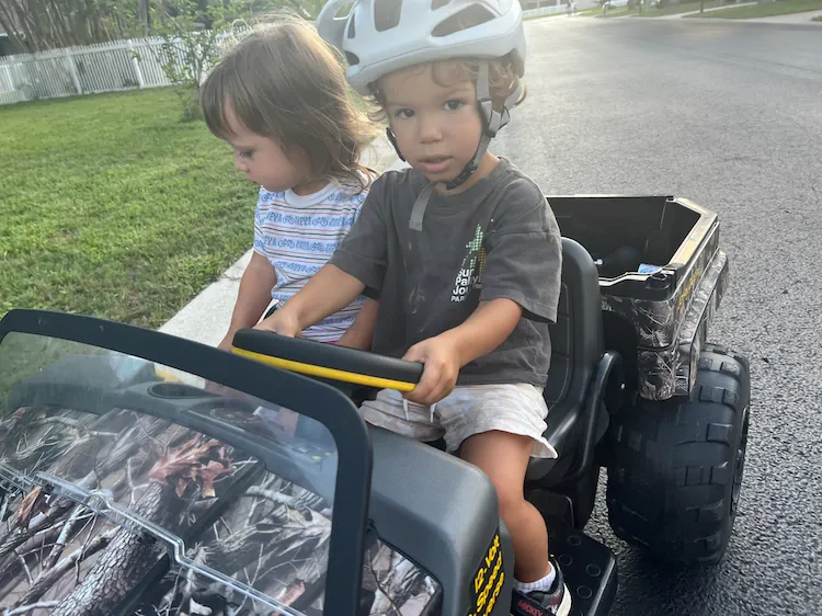 Two of the little ones behind the wheel of a toy jeep out in the neighborhood.