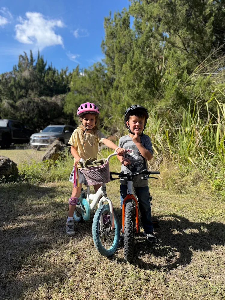 Two of the kids straddling their bikes on a pine-shaded Lee County trail.